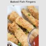 Overhead photo of baked fish fingers in a serving basket lined with parchment paper with a bowl of tomato sauce beside it