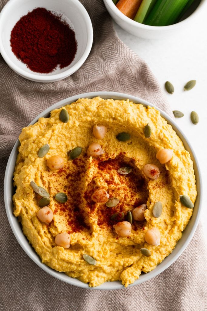 Overhead shot of pumpkin hummus in a white bowl topped with pumpkin seeds