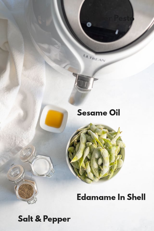 Overhead ingredient shot of ingredients required to make sesame edamame in the air fryer: edamame, sesame oil, salt and pepper
