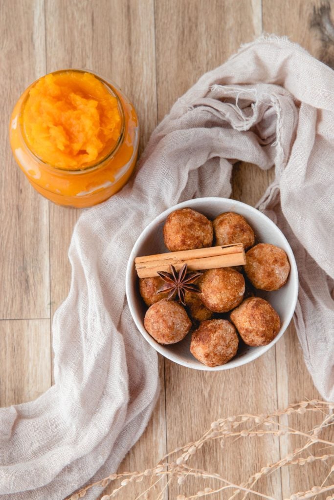 No Bake Pumpkin Balls piled in a white bowl and topped with cinnamon sticks and star anise with a jar of pumpkin puree in the background