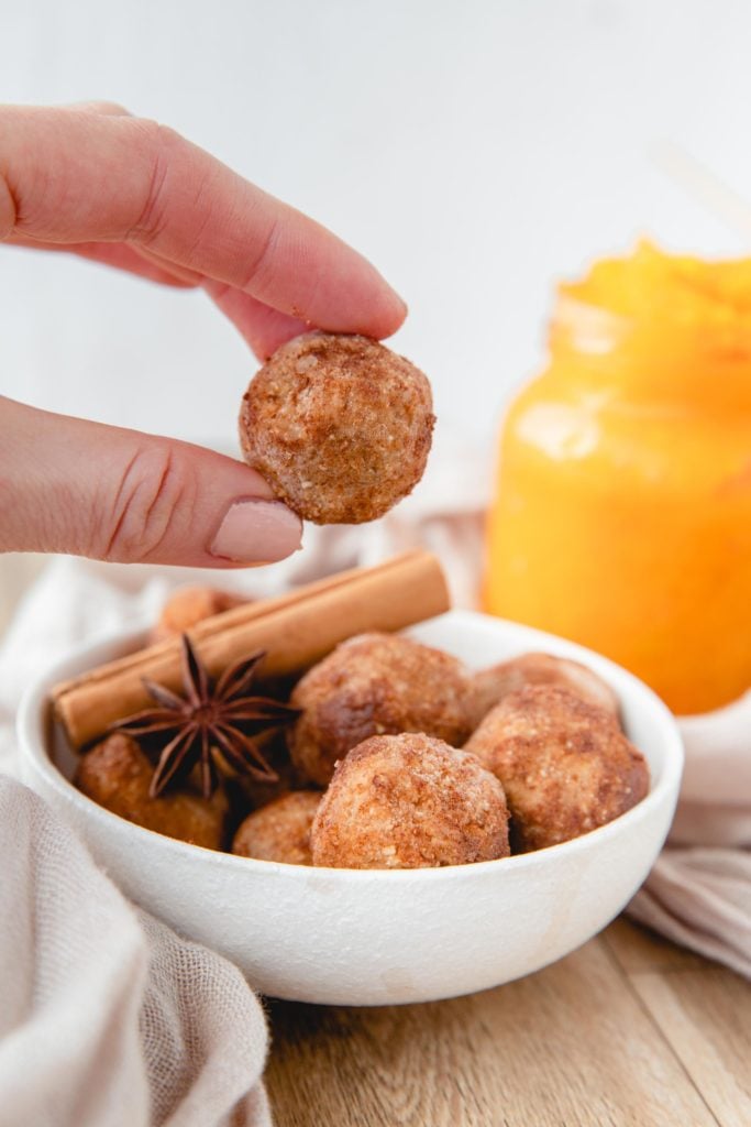 A hand picking up a pumpkin energy ball from a white bowl