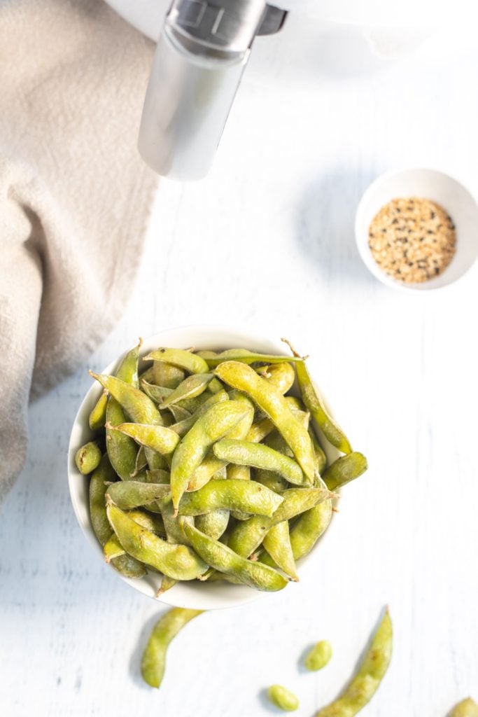 Cooked edamame in a small bowl with some shelled edamame surrounding it