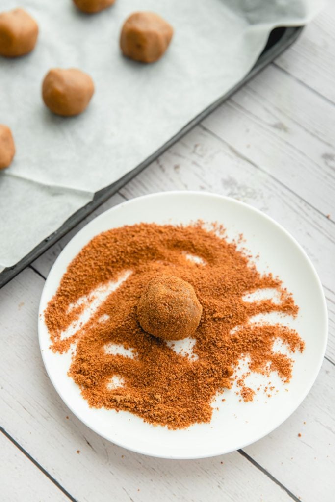 A plate of coconut sugar and unbaked gingersnap cookie dough balls being rolled in the sugar.