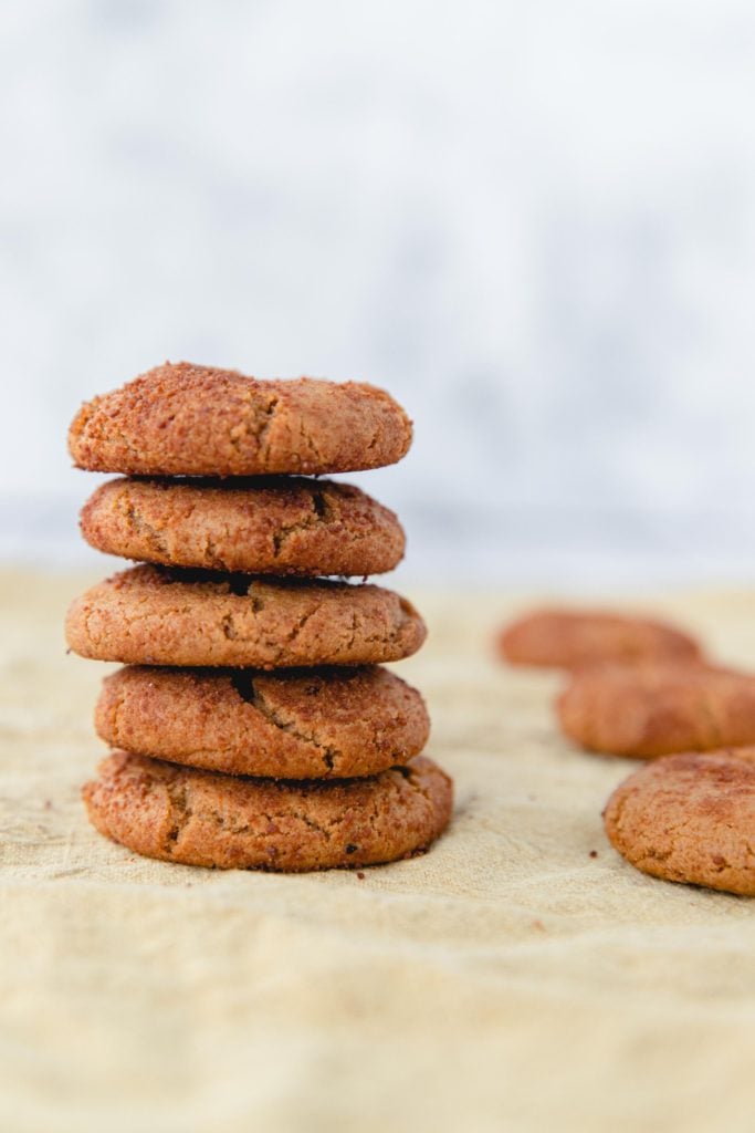 Gingersnap cookies without molasses stacked high on some parchment paper with a few spare cookies scattered in the background