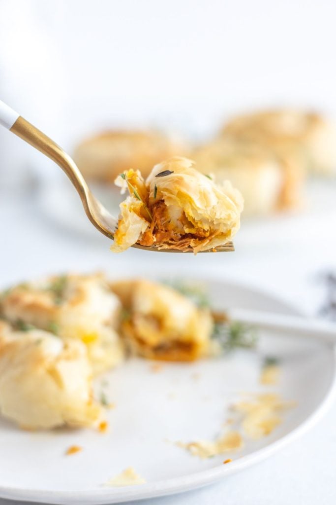 A forkful of pumpkin and feta savory hand pie being lifted from a white plate with a gold and white fork