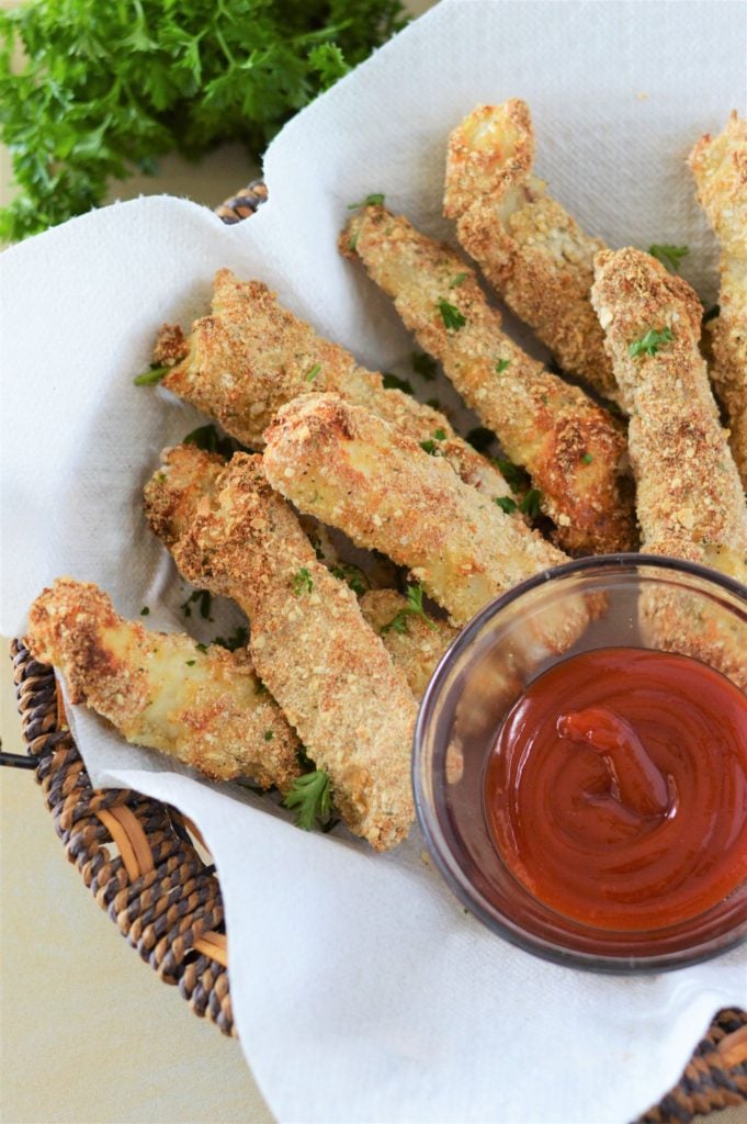 Baked fish fingers served in a basket lined with parchment paper with a small bowl of tomato sauce on the side