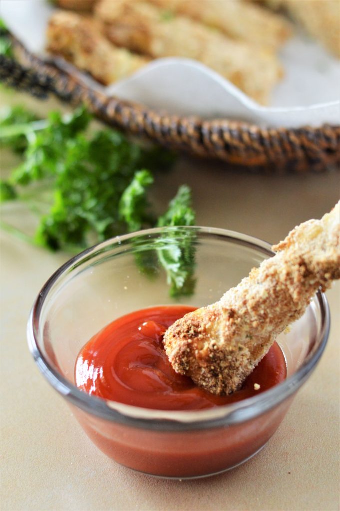 Up close shot of a fish stick being dunked in some tomato sauce served in a small glass bowl