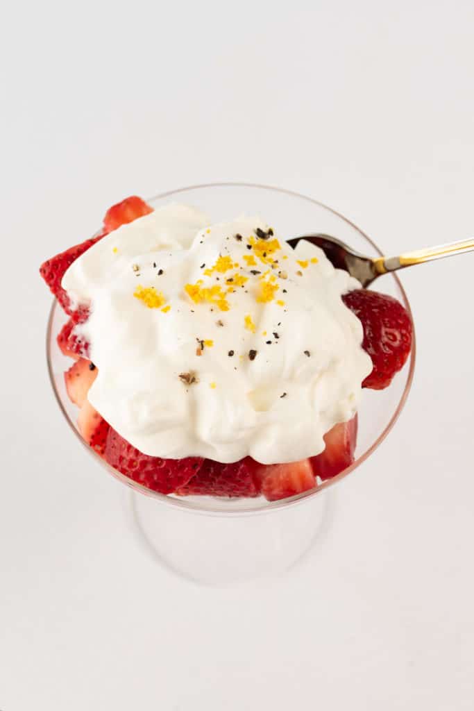 Overhead shot of orange liquor macerated strawberries topped with shipped cream and served in a fancy glass.