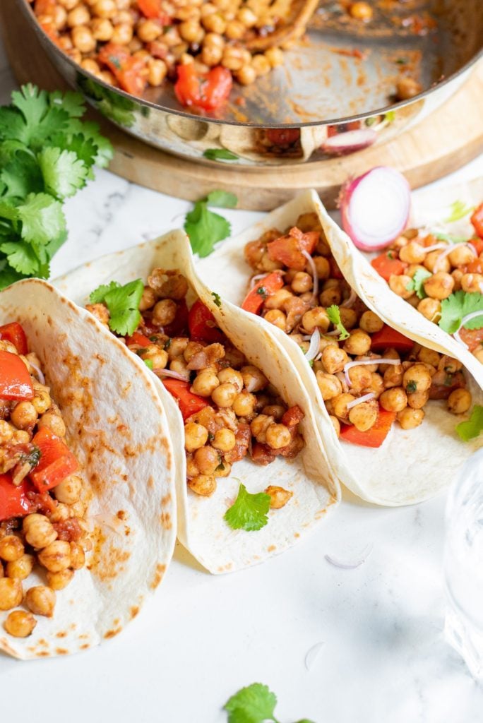 vegetarian tacos filled with bell peppers and chickpeas and lined up in a row in flour tortillas