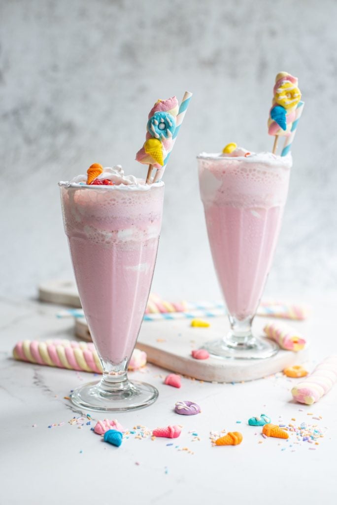 frontal shot of milkshakes in tall glasses topped with lots of candies and marshmallows