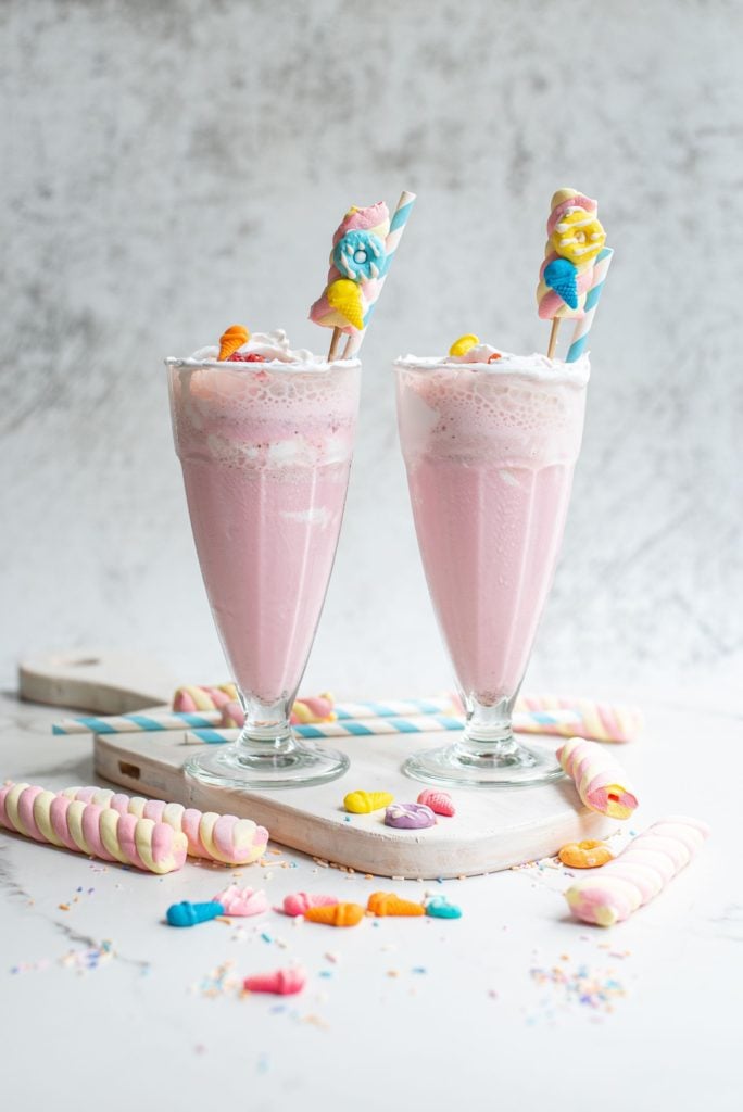 Two strawberry milkshakes with whipped cream and sprinkles served in tall glasses