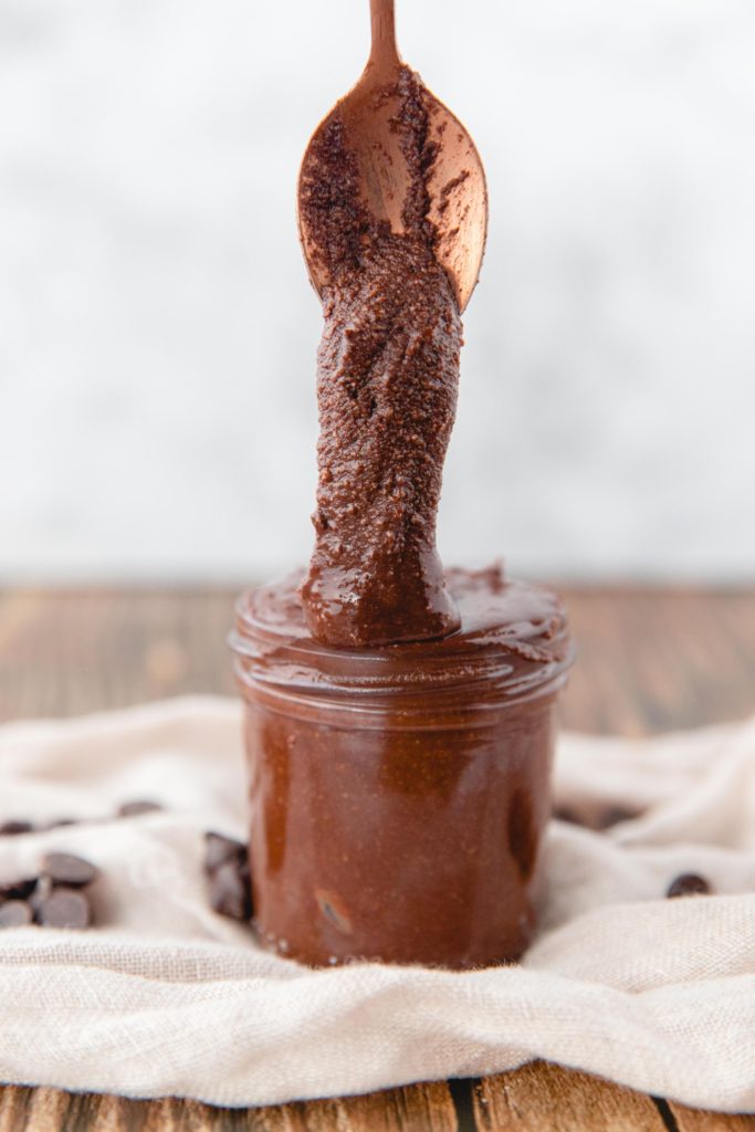 homemade nutella stored in a glass jar with a gold spoon dolloping some out