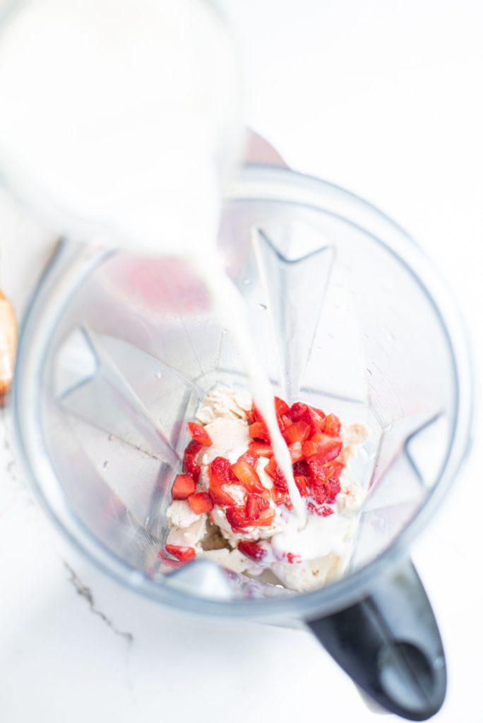 Overhead shot of ice cream, milk and crushed strawberries in a blender container