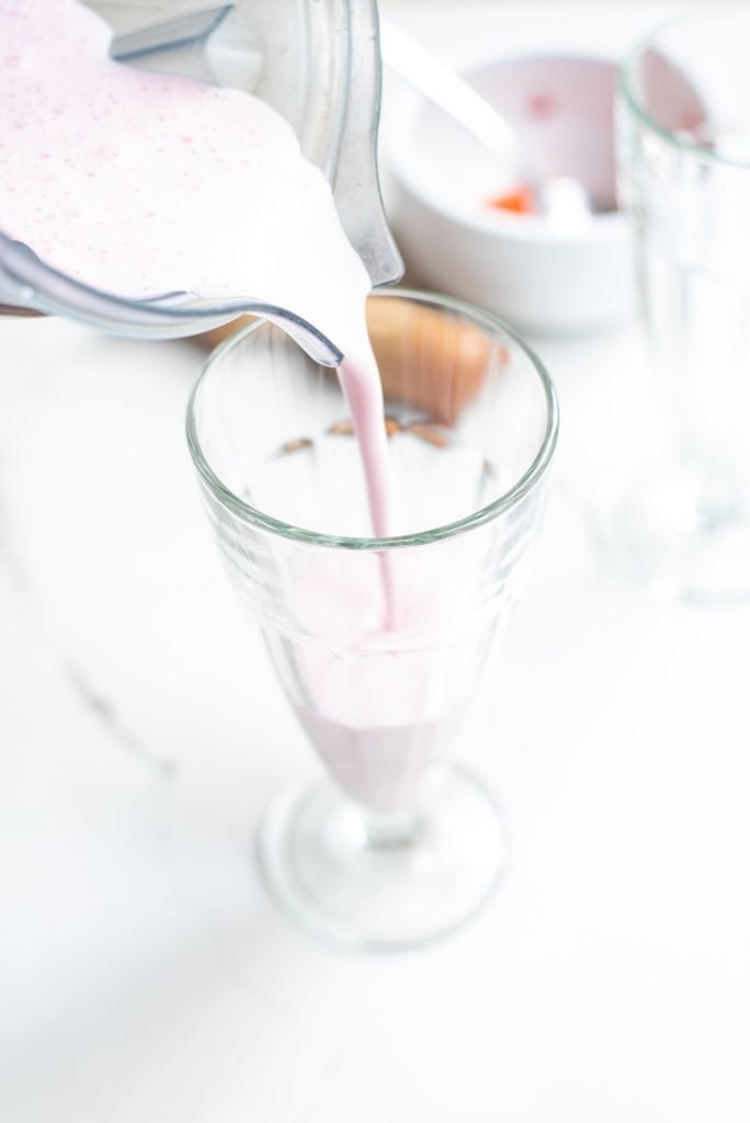 A milkshake being poured from a blender container into a tall glass
