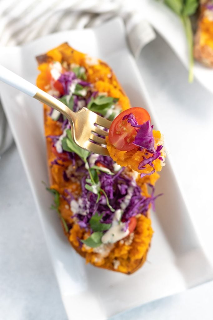 A hand holding a fork getting a spoonful of baked sweet potato and quinoa salad