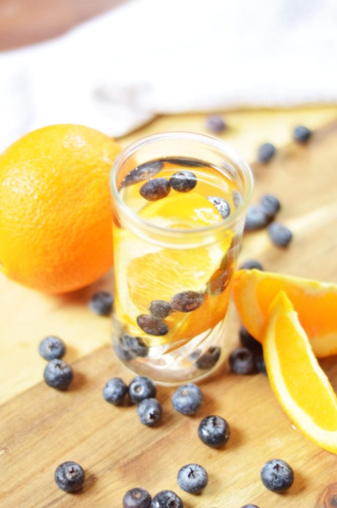 Blueberries and orange wedges served in a small glass with extra blueberries and oranges scattered around