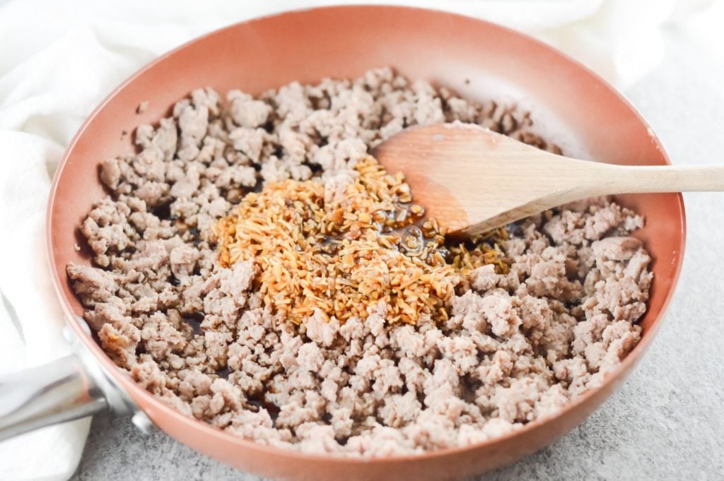 pork mince in a skillet with sauce being added and stirred