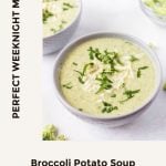 Two bowls of green soup served up in white bowls with some slices of fresh bread on a chopping board in the background, and broccoli florets spread around