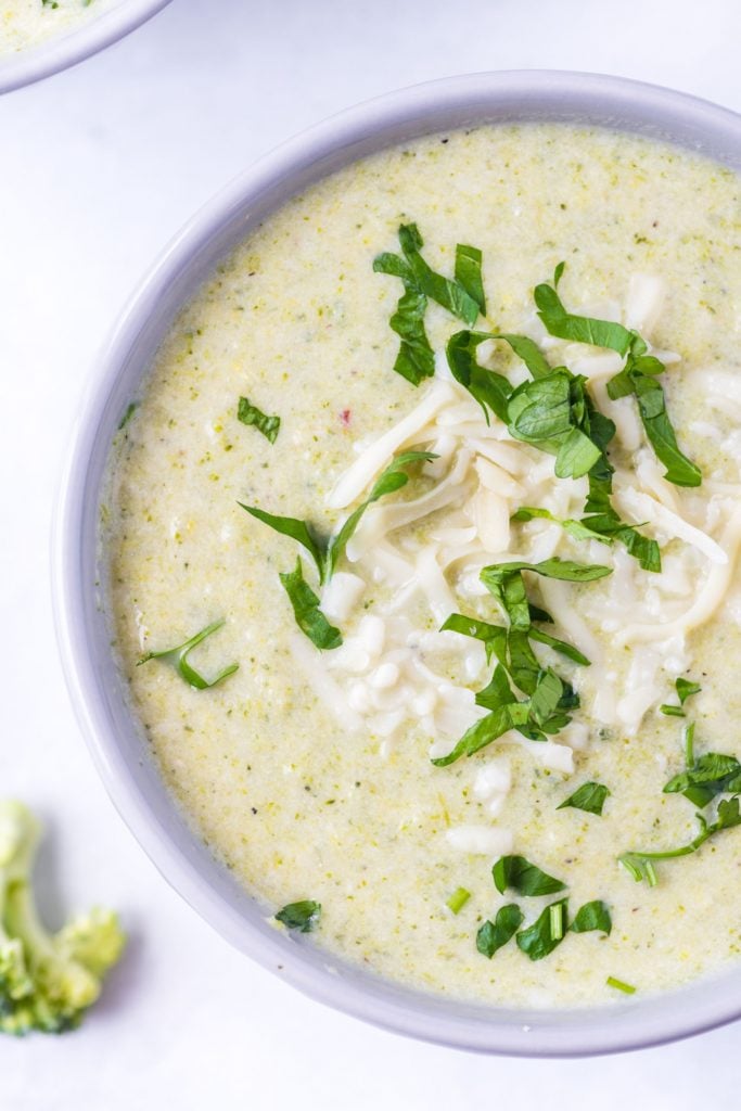 Up close overhead shot of a light green soup served in a white bowl and sprinkled with cheese and parsley