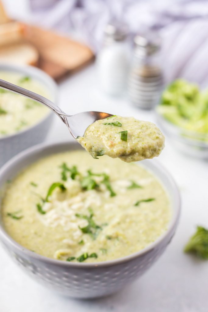 A spoon serving up some broccoli soup from a white bowl