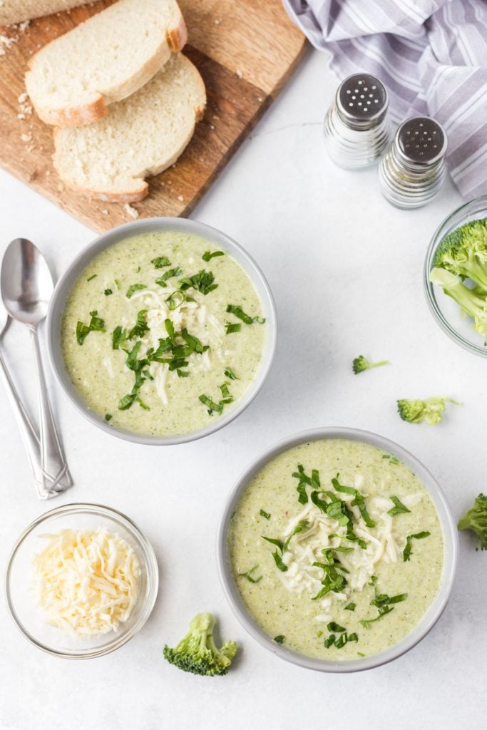 Overhead shot of a light green soup served into 2 white bowls with some cheese and bread