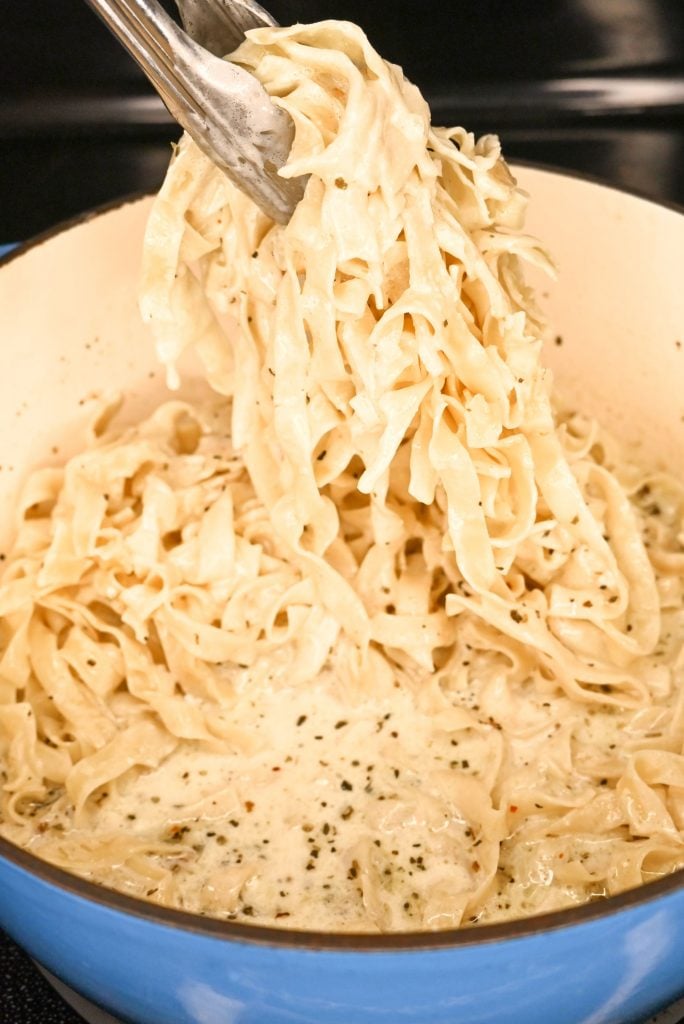 Shot of a creamy fettuccine Alfredo being lifted from a blue crockpot with some tongs