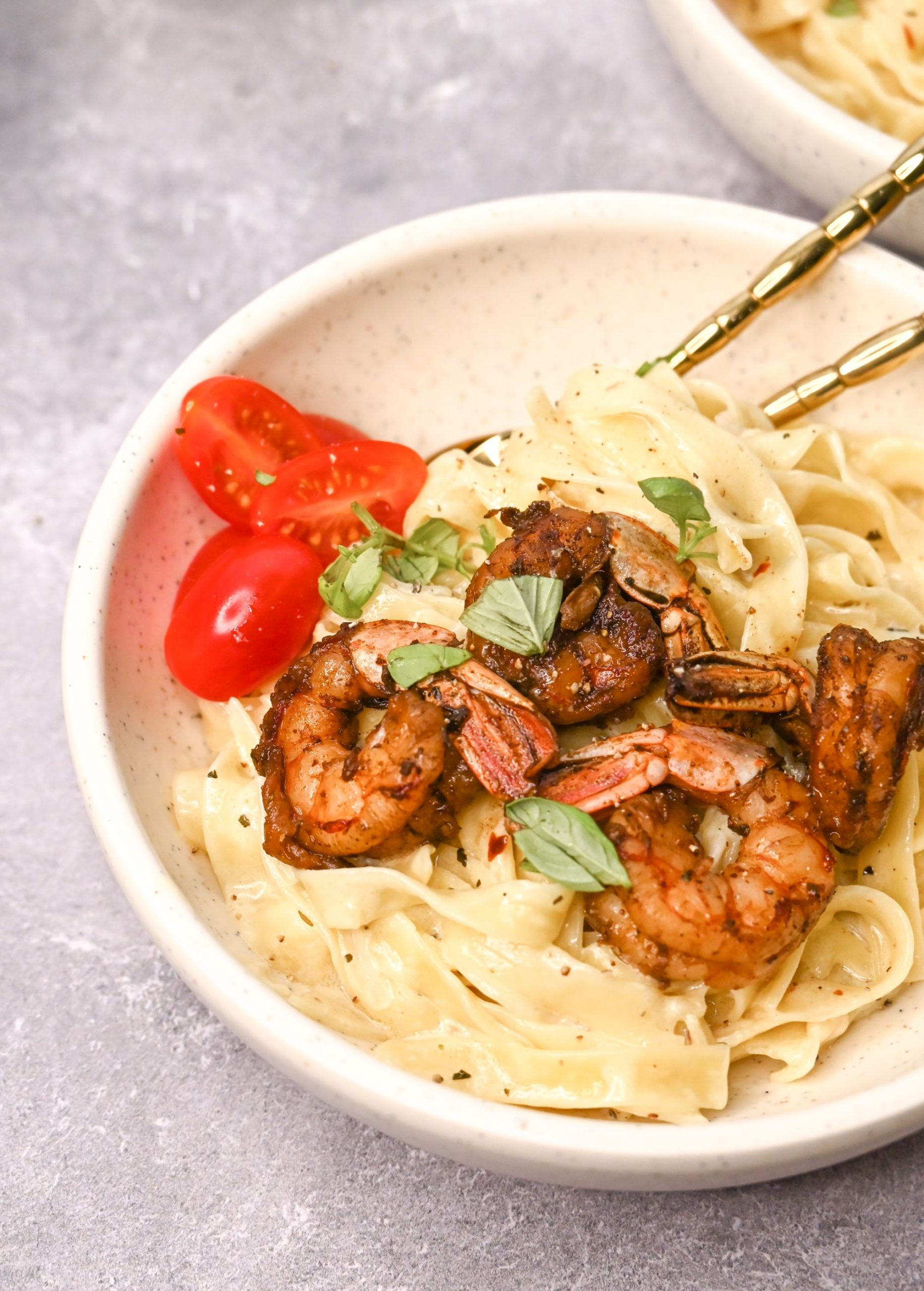 Cajun shrimp on top of some creamy pasta served in a white bowl with chopped cherry tomatoes on the side