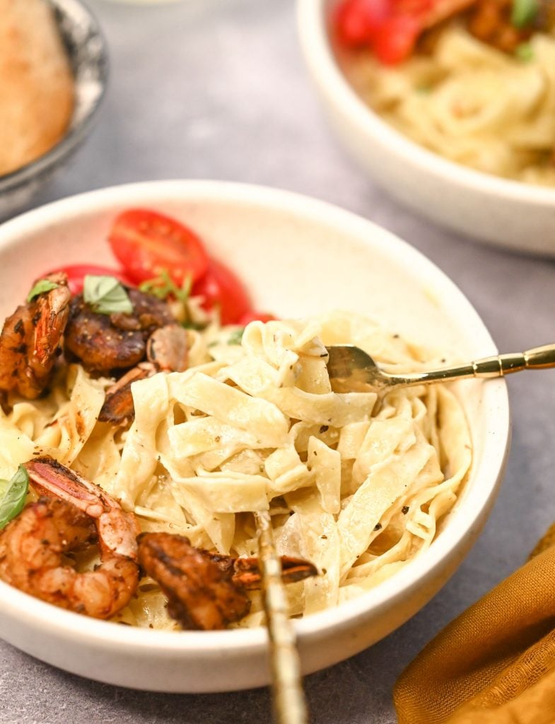 Two forks in a bowl of creamy cajun shrimp pasta scooping up the fettuccine