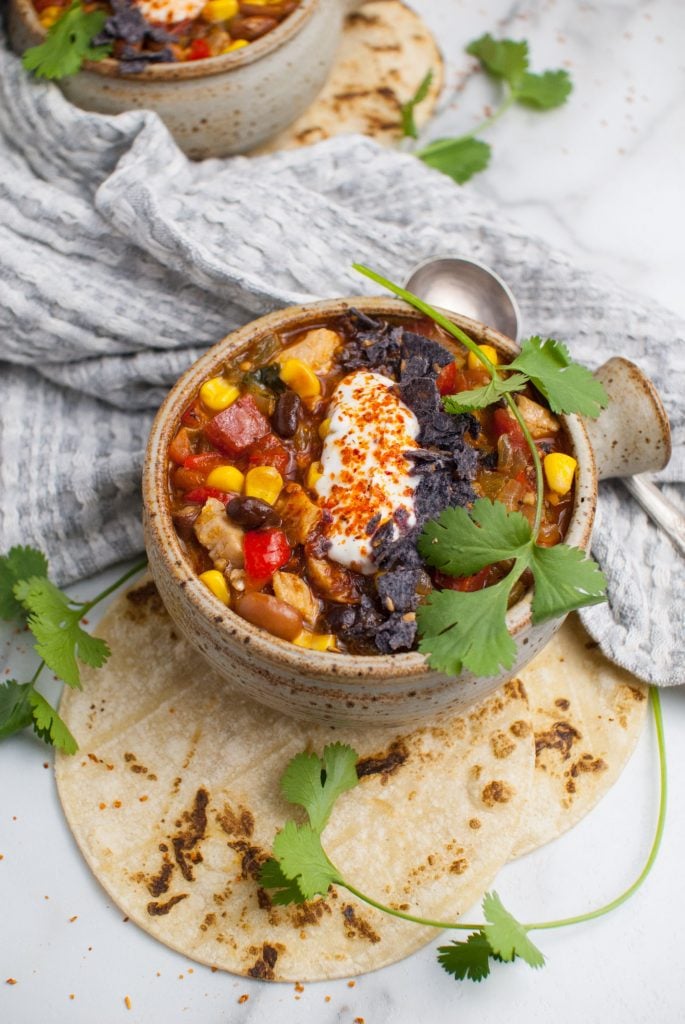 Up close shot of leftover turkey enchilada soup served in a rustic bowl and topped with sour cream and tortilla chips