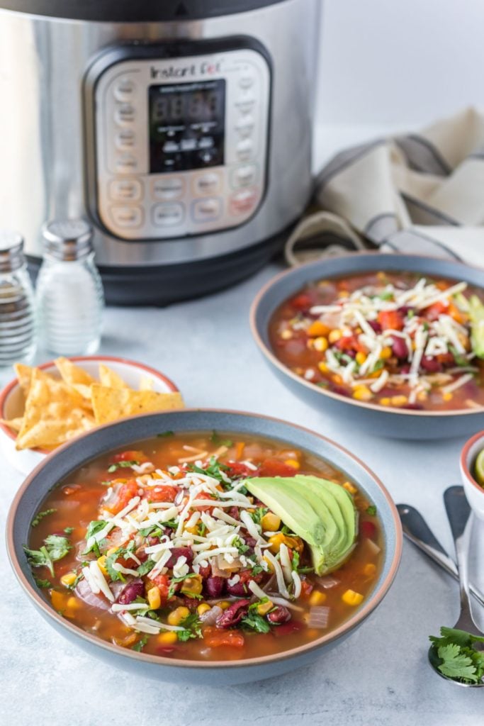 Vegetarian taco soup loaded up with avocado and shredded cheese with an instant pot in the background along with cilantro and corn chips