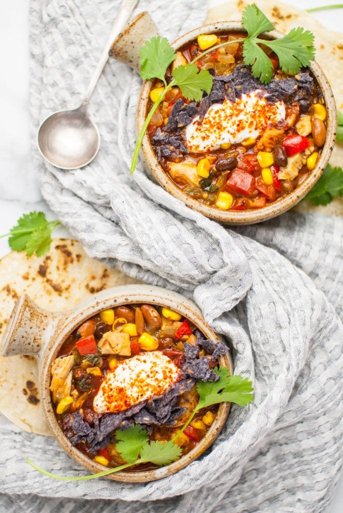 Overhead shot of enchilada soup served up in a rustic bowl and grey linen with a silver spoon and some fresh tortillas in the background