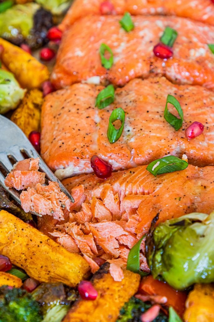 Up close shot of Salmon broccoli and sweet potatoes on a baking sheet with a fork pulling the salmon apart