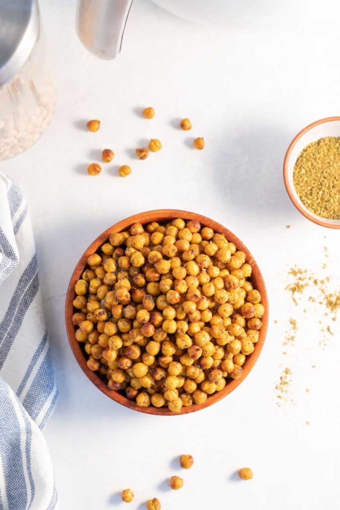 overhead shot of air fryer zaatar chickpeas served in a wooden bowl against a white background with loose crispy chickpeas and zaatar sprinkled around