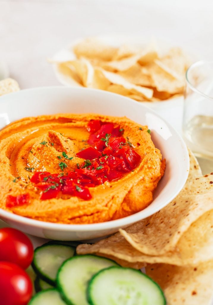 A smooth and creamy homemade hummus topped with chopped red bellp peppers and served in a white bowl