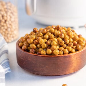 overhead shot of air fryer chickpeas coated in zaatar served in a wooden bowl against a white background with some loose chickpeas and a jar of dried garbanzo beans in the background