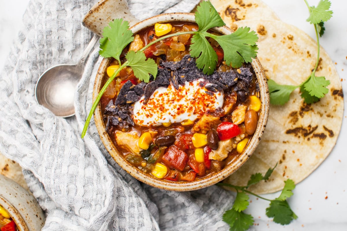 Up close shot of leftover turkey enchilada soup served in a rustic bowl and topped with sour cream and tortilla chips