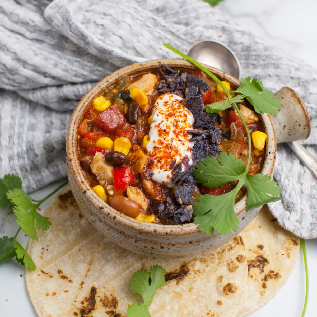 Up close shot of leftover turkey enchilada soup served in a rustic bowl and topped with sour cream and tortilla chips