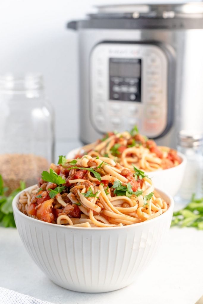 Two white bowls filled with spaghetti and vegetarian bolognese in front of an instant pot