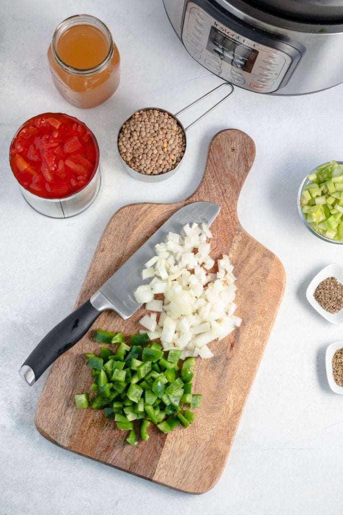 Overhead shot of a chopping board with chopped onions and bell peppers, and small containers surrounding the chopping board containing all of the other ingredients