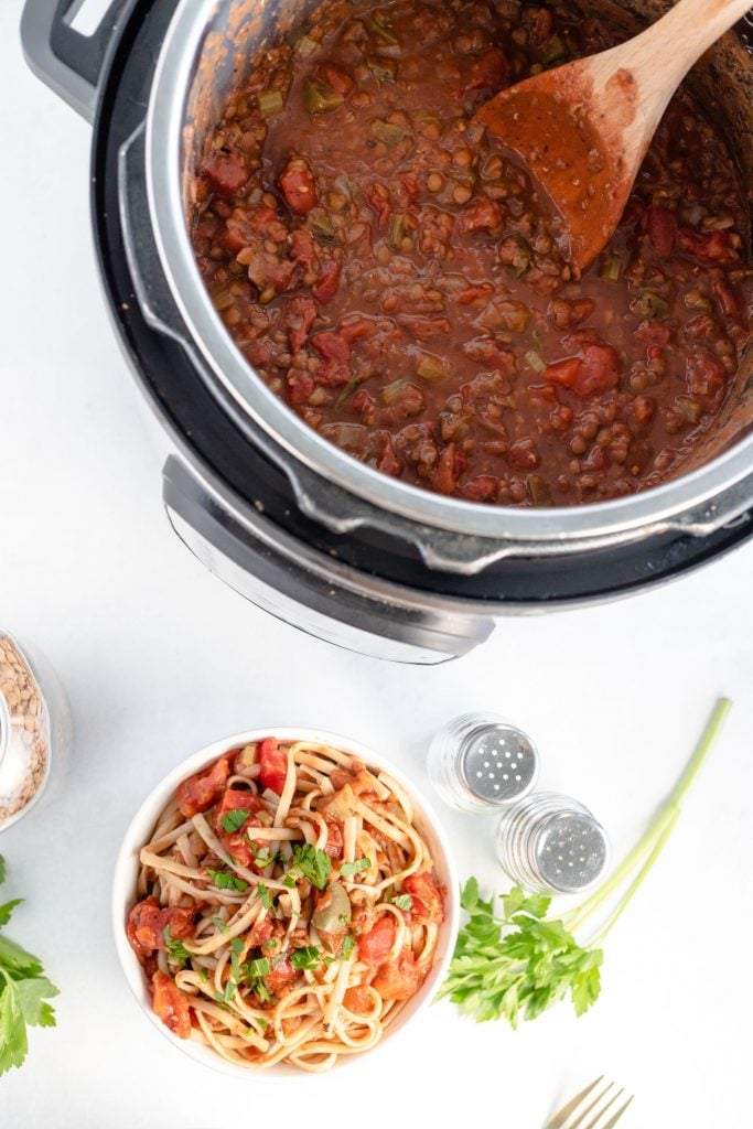 Instant pot full of vegetarian bolognese sauce and a small white bowl with pasta and bolognese sauce mixed together. There is salt and pepper and fresh parsley in the background