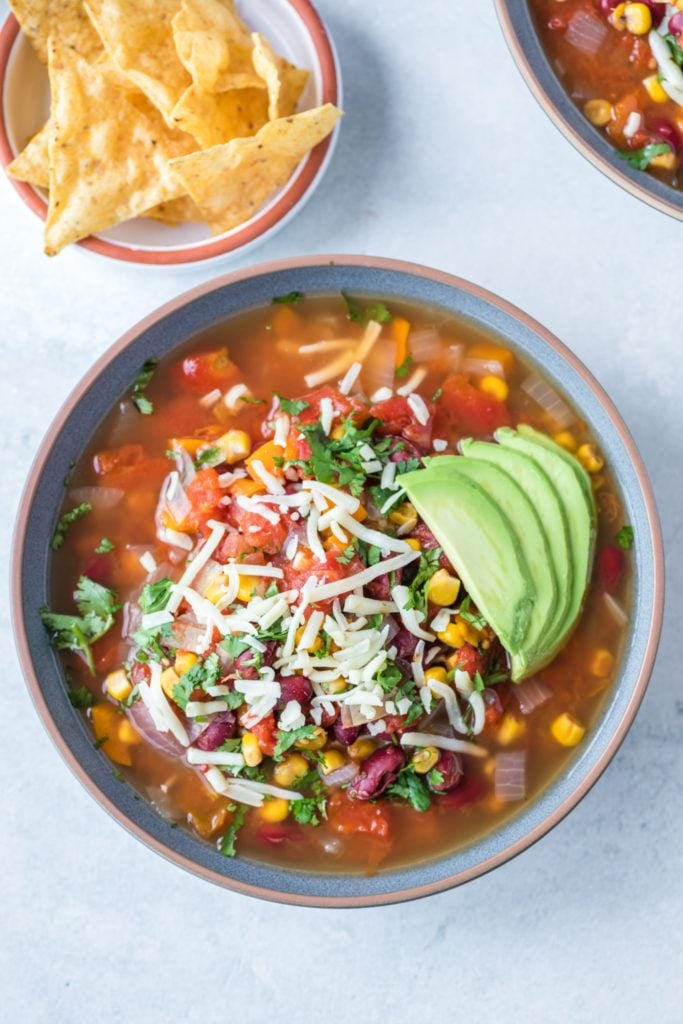 Overhead shot of Vegetarian taco soup loaded up with avocado and shredded cheese 
