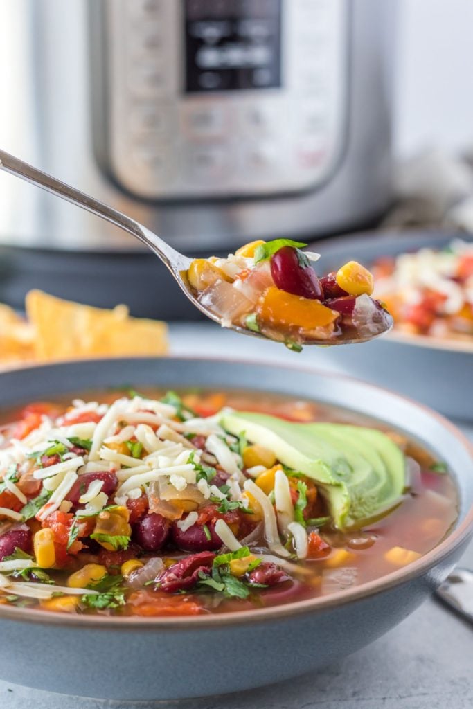 Instant pot soup served in a blue bowl and being scooped with a spoon with an instant pot in the background