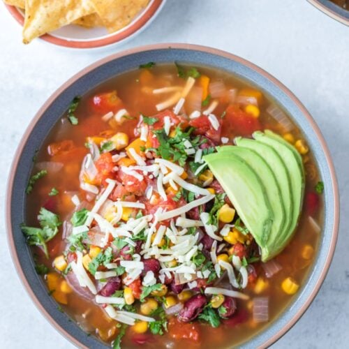 Overhead shot of Vegetarian taco soup loaded up with avocado and shredded cheese