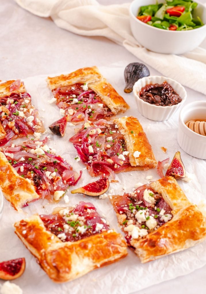 puff pastry onion appetizer chopped into 6 slices against a white background with a bowl of salad
