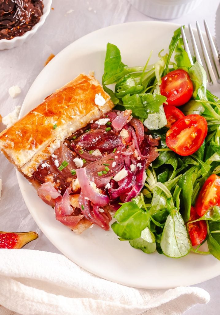 puff pastry tart served on a white plate alongside a green salad and some tomatoes
