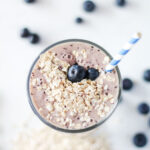 banana blueberry smoothie served in a tall glass with a blue and white straw