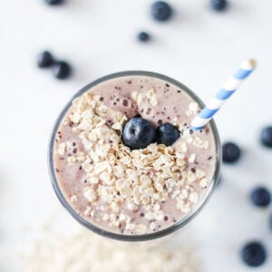 banana blueberry smoothie served in a tall glass with a blue and white straw