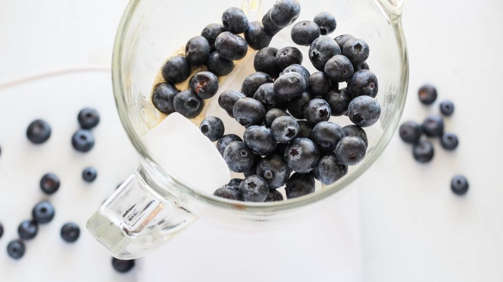 blueberries, milk, protein powder and ice in a glass blender container
