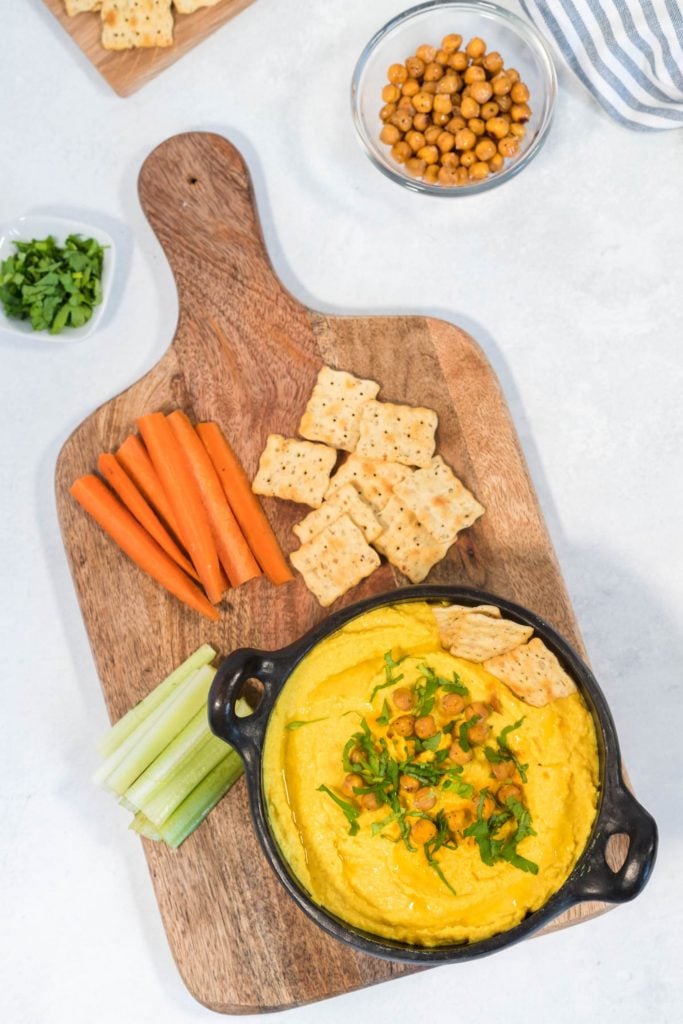 Overhead shot of homemade hummus topped with chickpeas and parsley and served with veggie sticks and crackers