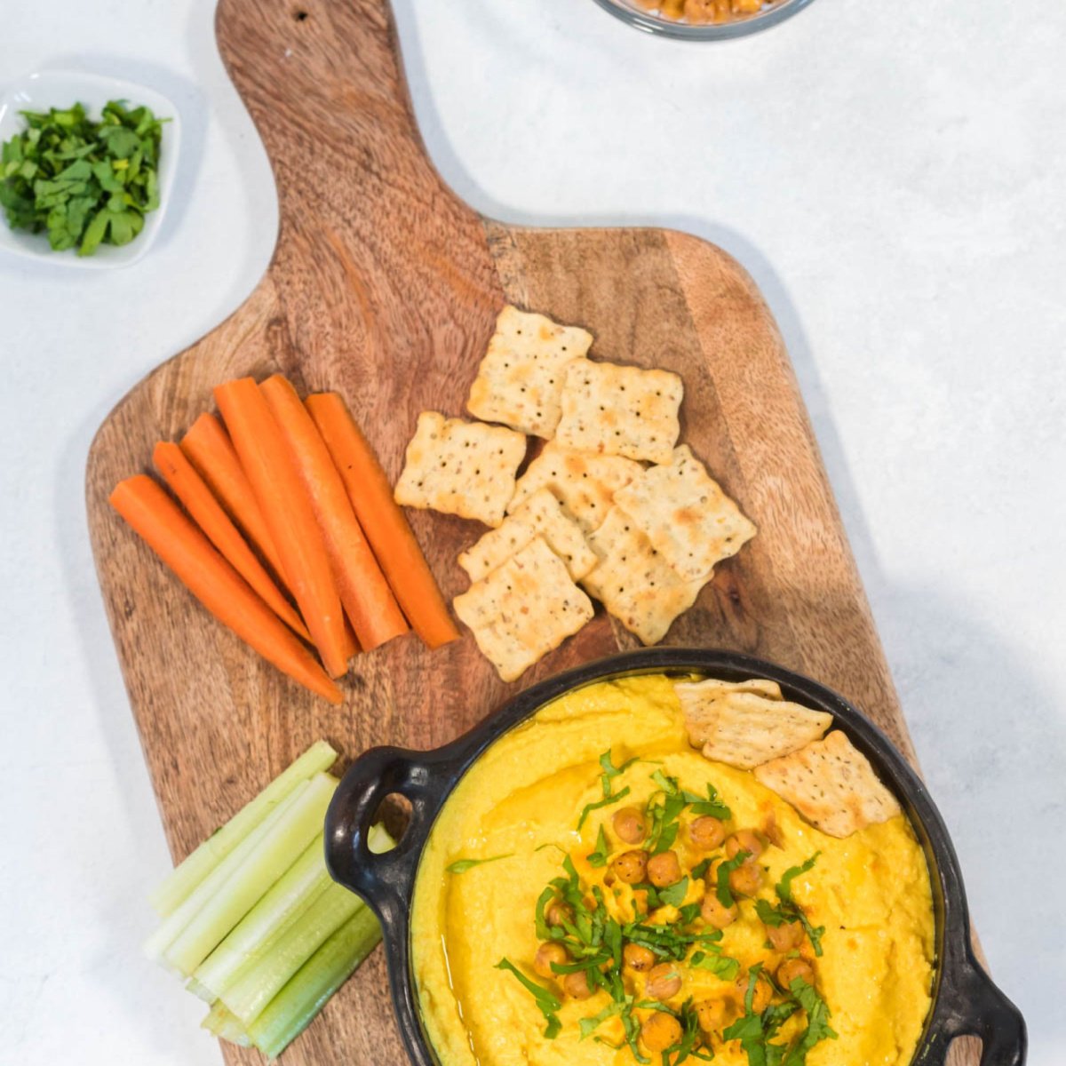 overhead shot of turmeric hummus served in a black bowl with a side of veggie sticks and crackers